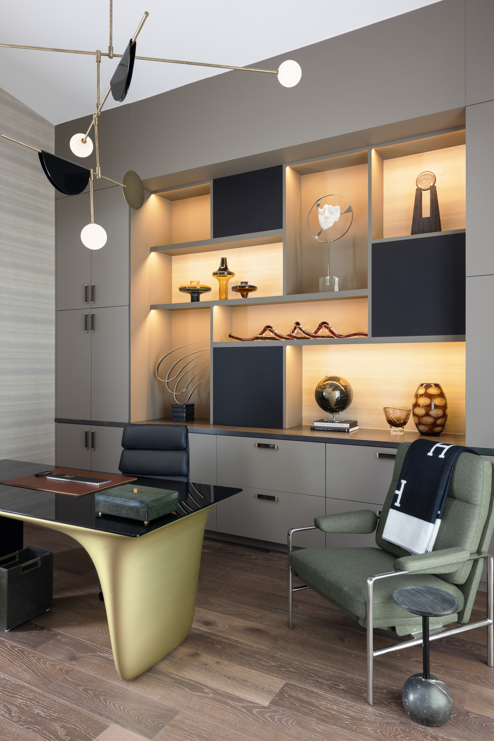 Home office with brass mobile chandelier and backlit display shelving