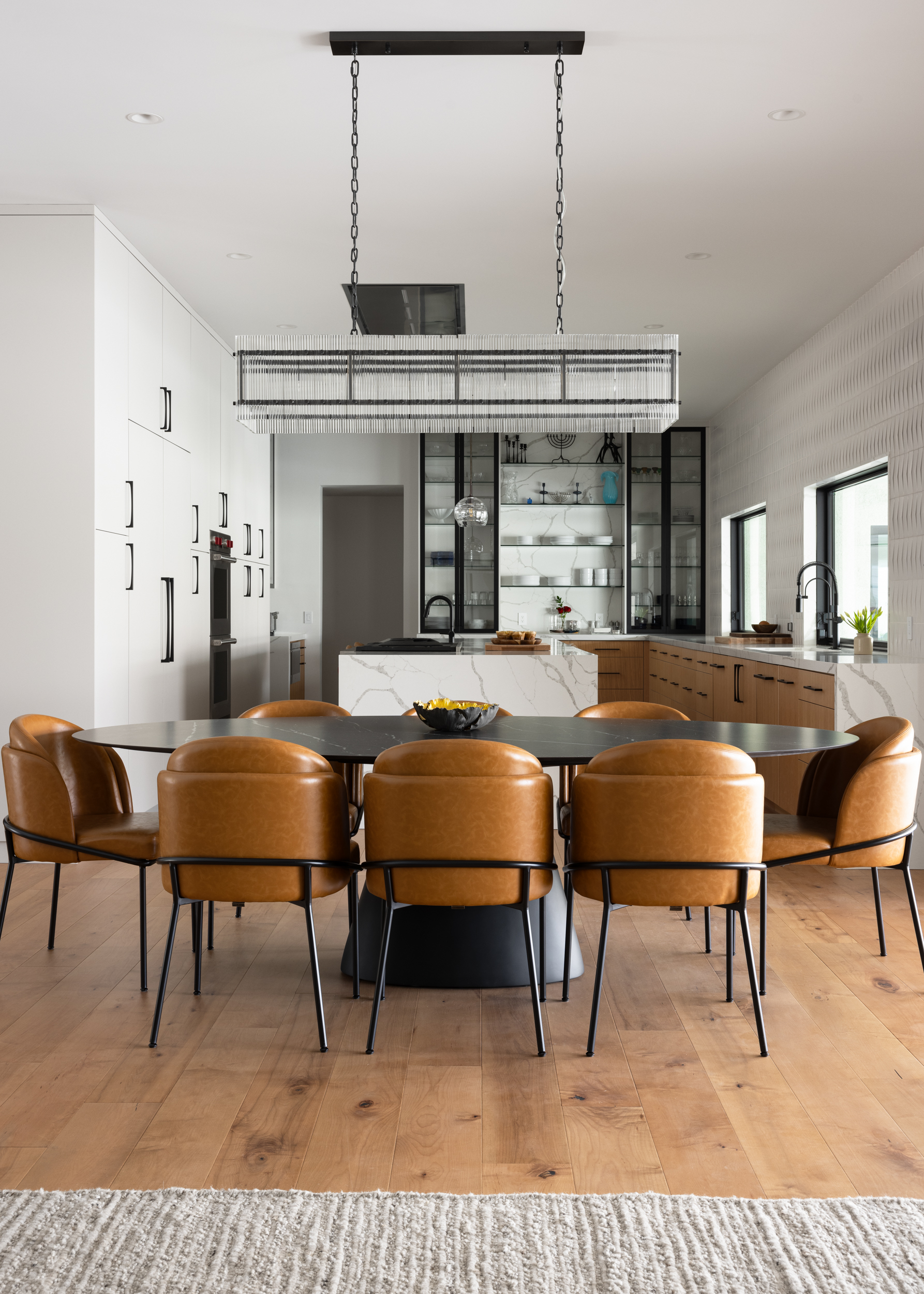 Dining room with oval stone table, cognac leather chairs, and linear chandelier